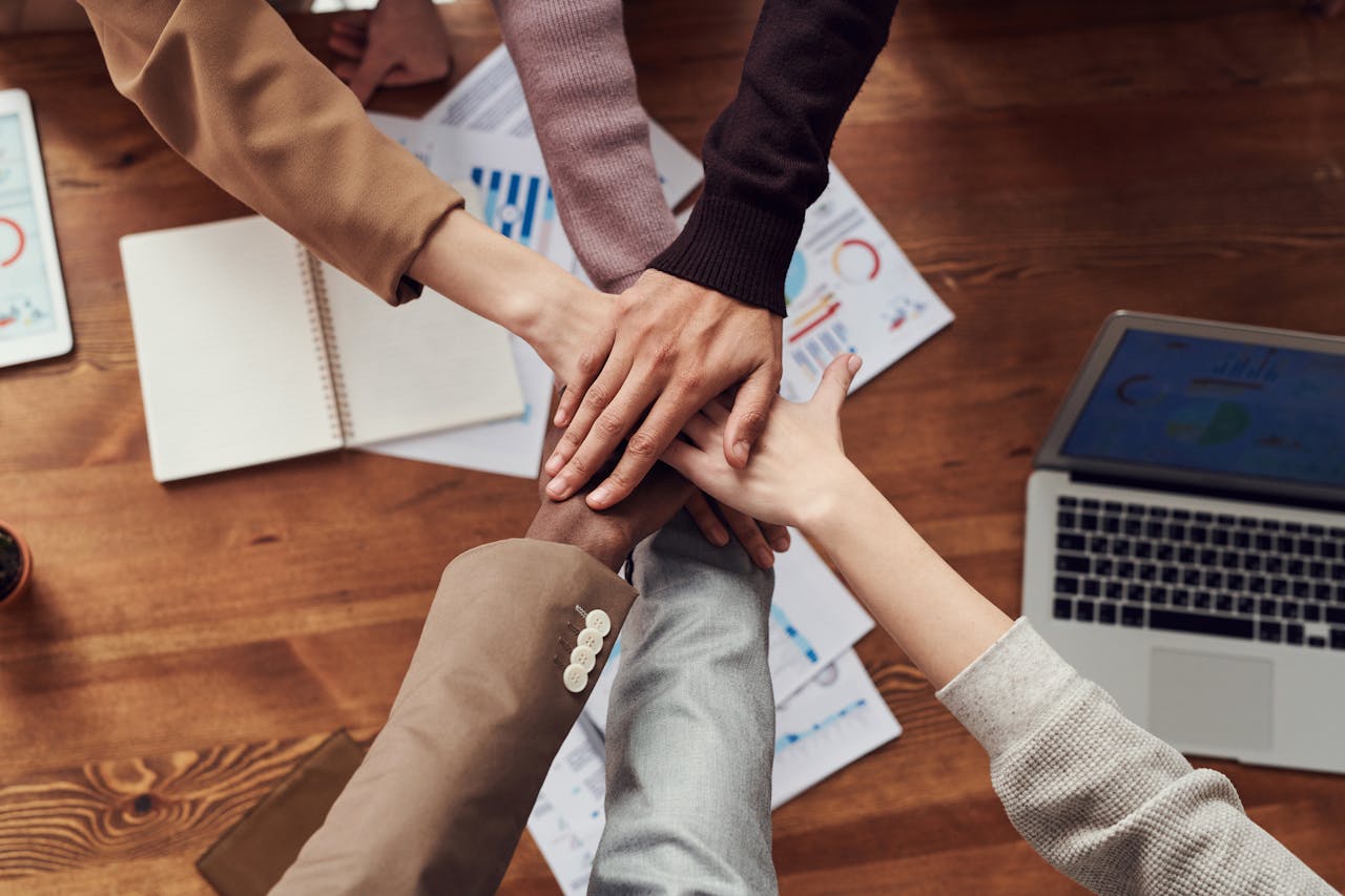 about-us Diverse professionals unite for teamwork around a wooden table with laptops and documents.