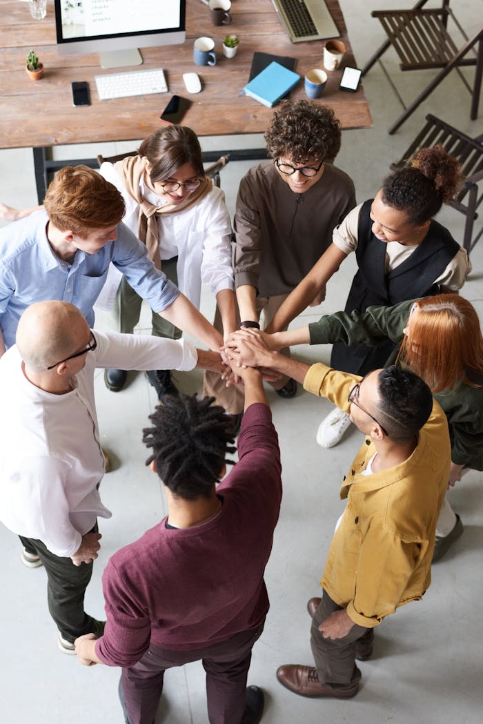 heros-img A diverse group of professionals joins hands in a team-building exercise indoors.